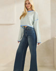 Side view of BTTRMMT Blue Rumi Pop Stripe Knit, pastel blue and yellow cropped sweater styled with dark wide-leg jeans.
