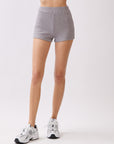 Model wearing BTTRMMT Lia Ribbed Shorts in light gray, featuring a fitted rib-knit texture and high-rise waist, styled with sneakers.