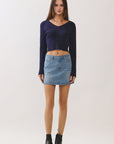 Model wearing BTTRMMT navy ribbed V-neck knit top paired with light wash denim mini skirt, studio front view.