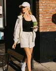 Model wearing BTTRMMT chill zip hoodie and shorts set with black tank and cap, walking outside with a matcha drink.