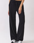 BTTRMMT Black Yuna Soft Wide Leg Pants front view with a drawstring waistband, relaxed drape, and casual fit styled with sneakers.