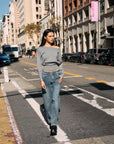 Model walking in BTTRMMT Gray Tessa Boatneck Sweater, off-shoulder knit with jeans and black loafer.