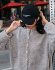 BTTRMMT black Better Moments cap styled with a soft taupe button-up cardigan during a casual city moment."