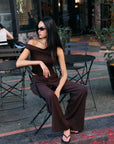 Model wearing the BTTRMMT Daniela Off-Duty Set in brown, seated outdoors in a one-shoulder ruched top and wide-leg pants.
