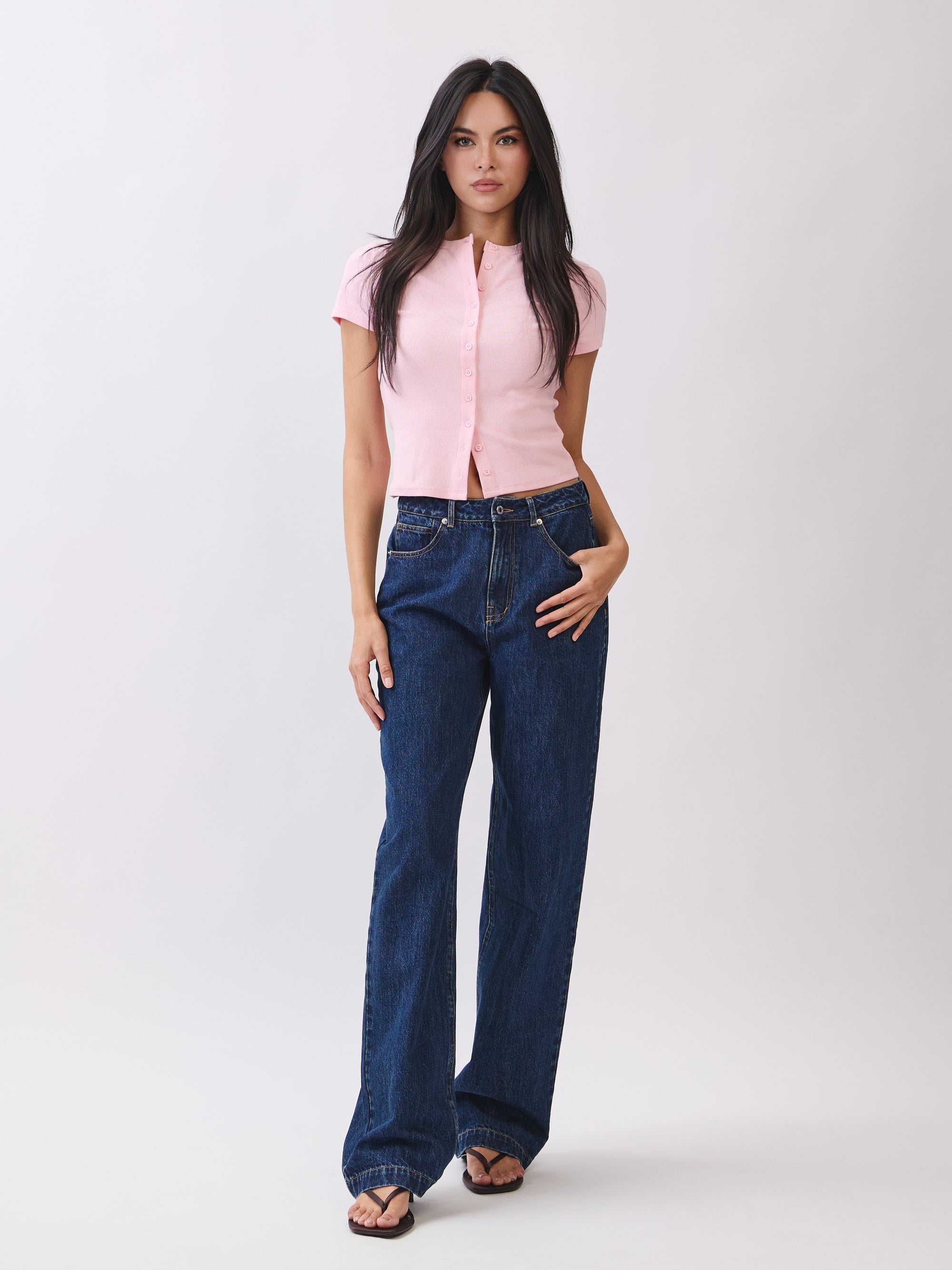 Full-body view of model wearing BTTRMMT Emery Straight Jean in dark blue denim, styled with a pink button-up knit top