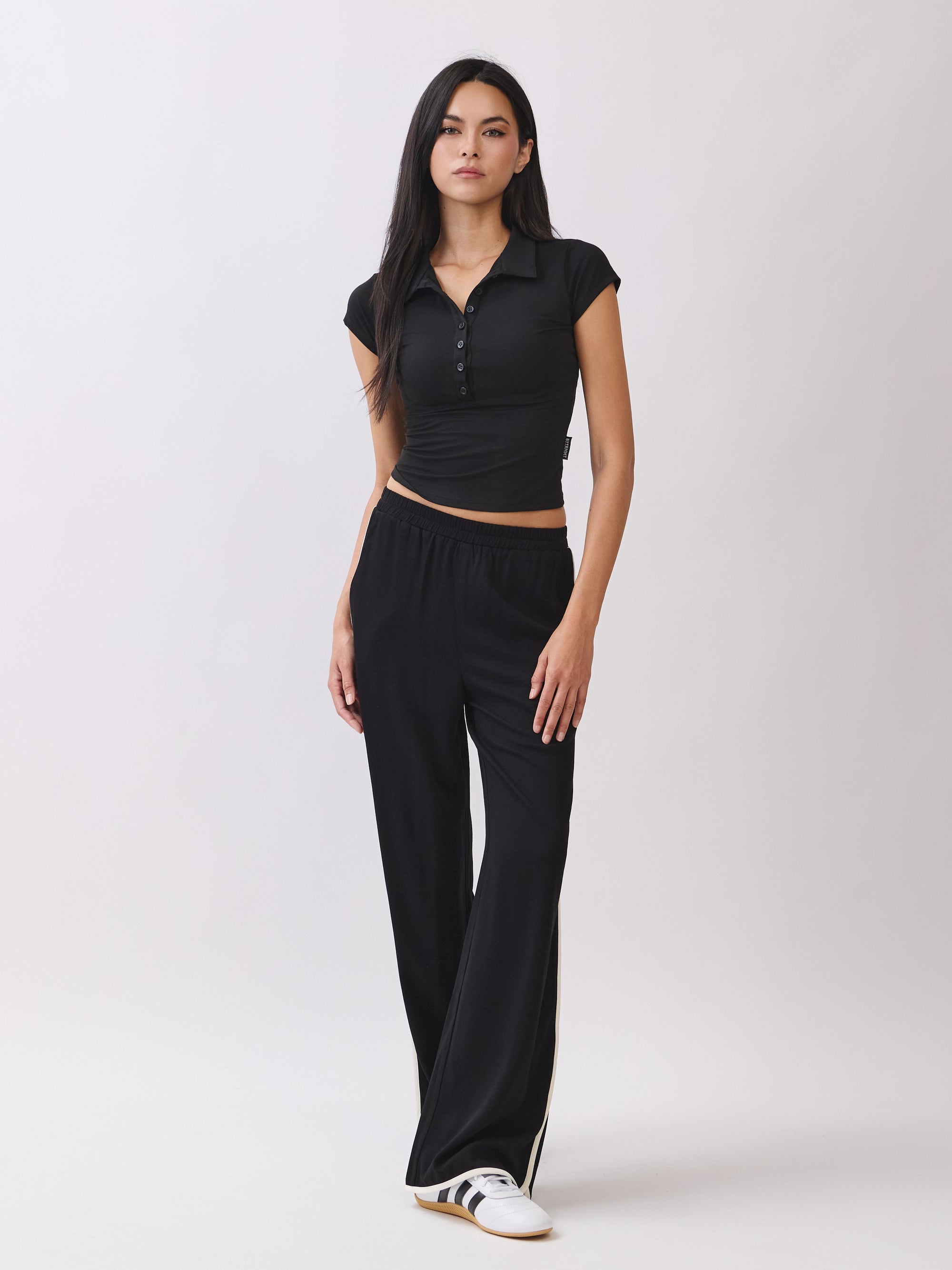 Model wearing the Nova Contrast Trim Pants in black with white side stripes, paired with a fitted black collared top.