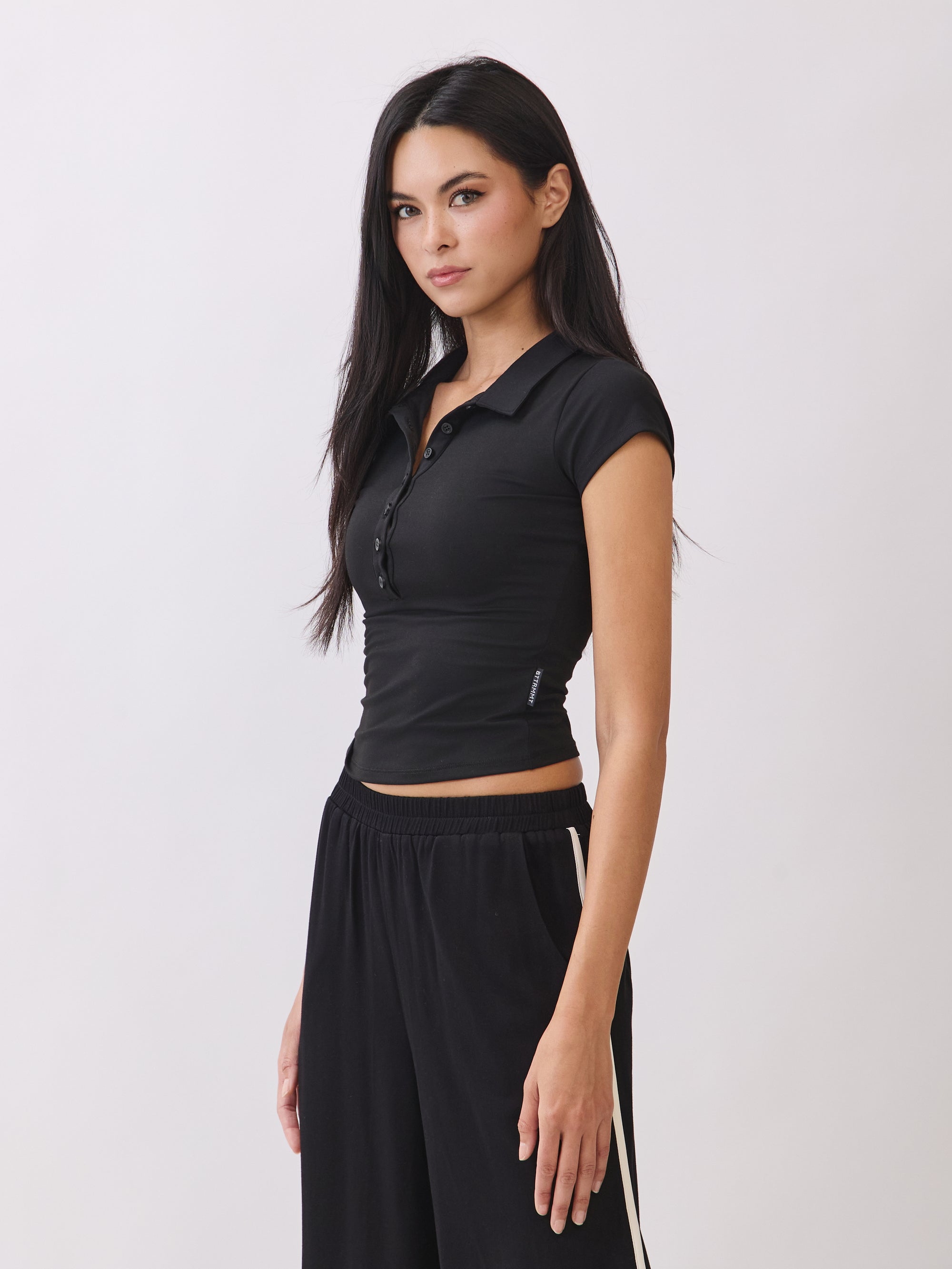 Side view of the BTTRMMT Black Eliza Fitted Polo Top, showing its slim stretch fit, cap sleeves, and clean, minimal everyday style.