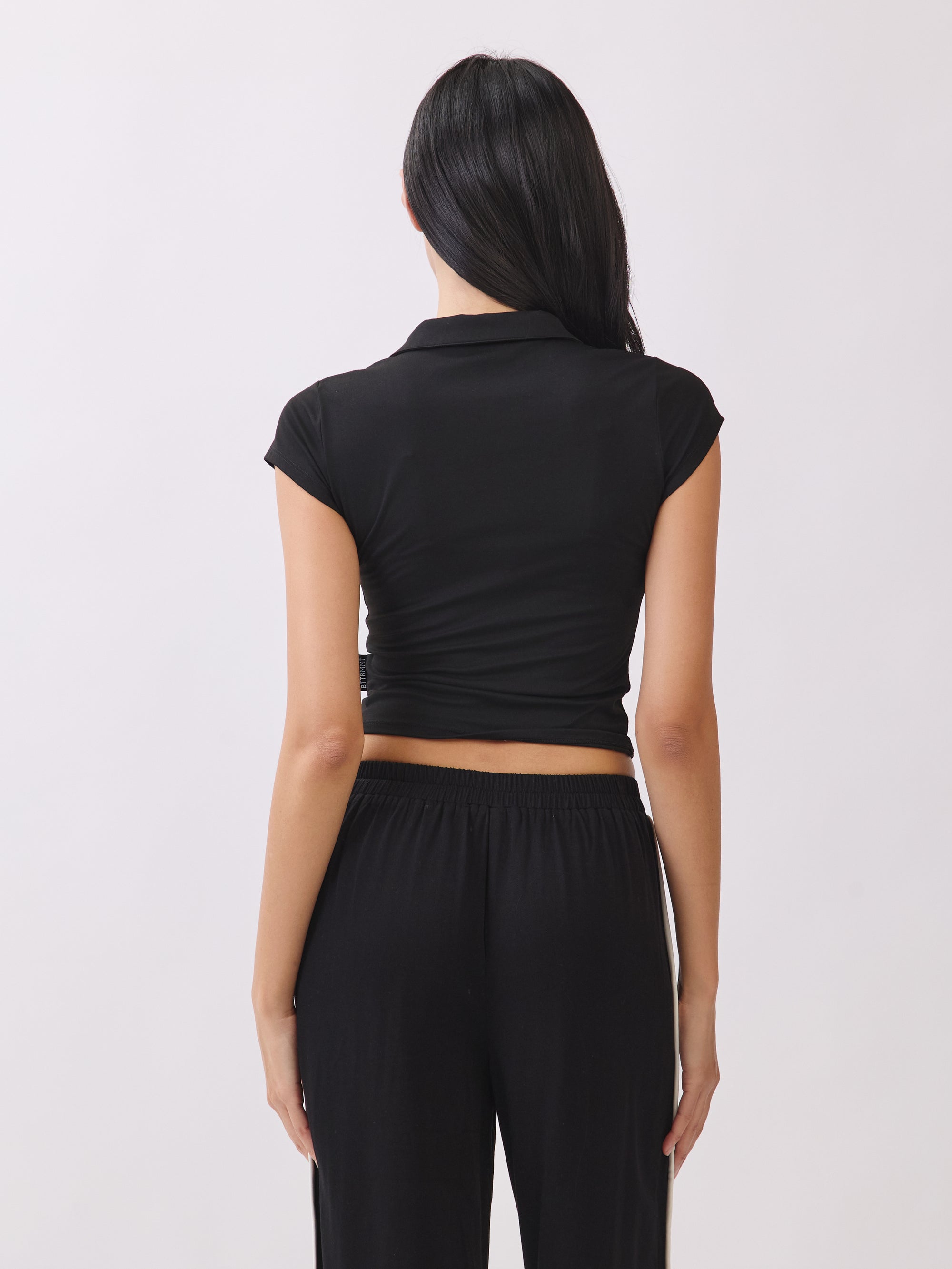 Back view of the BTTRMMT Black Eliza Fitted Polo Top, showing its slim stretch fit, cap sleeves, and clean, minimal everyday style.