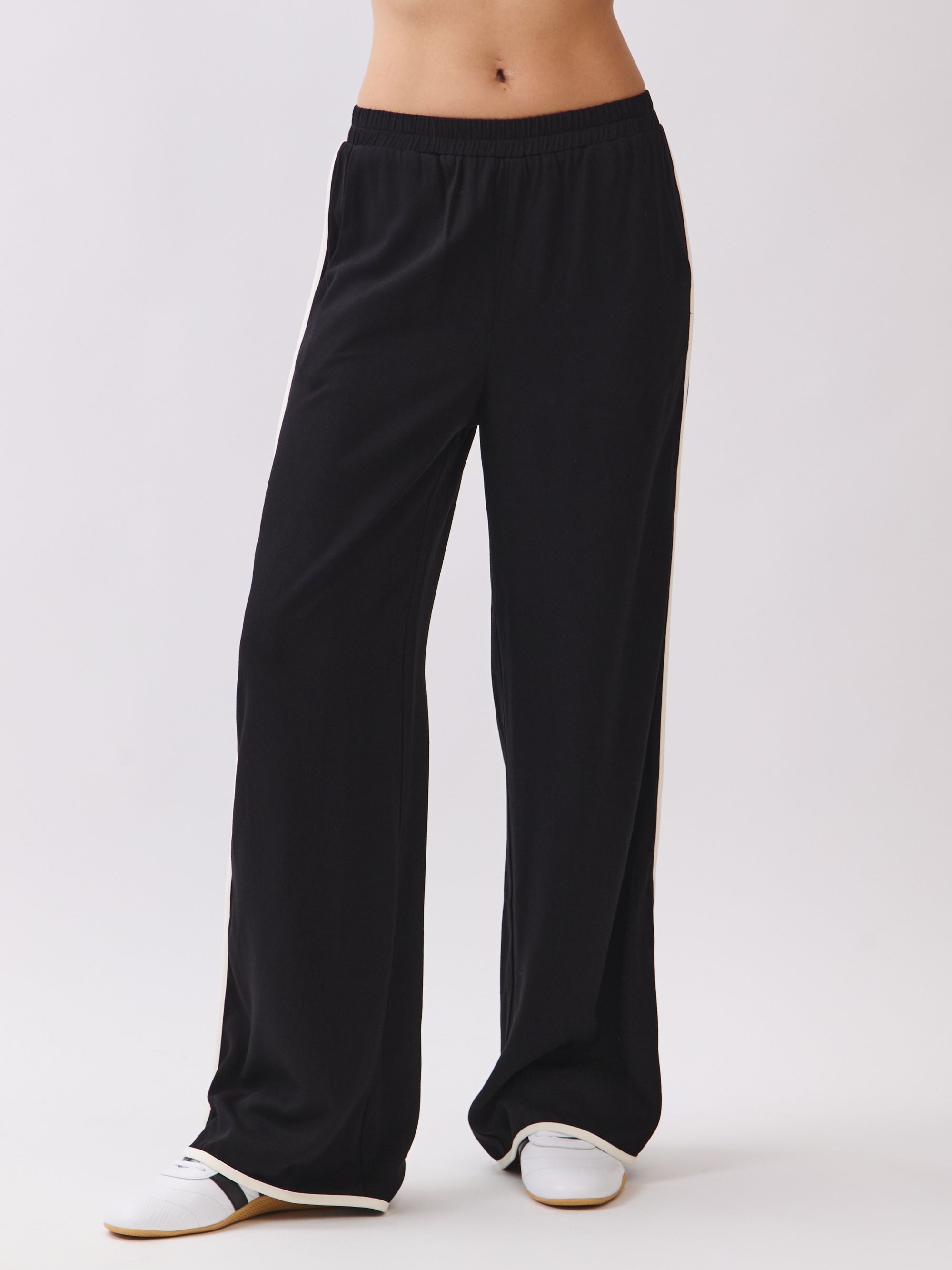 Model wearing the Nova Contrast Trim Pants in black with white side piping, styled with sneakers for a casual sporty look.