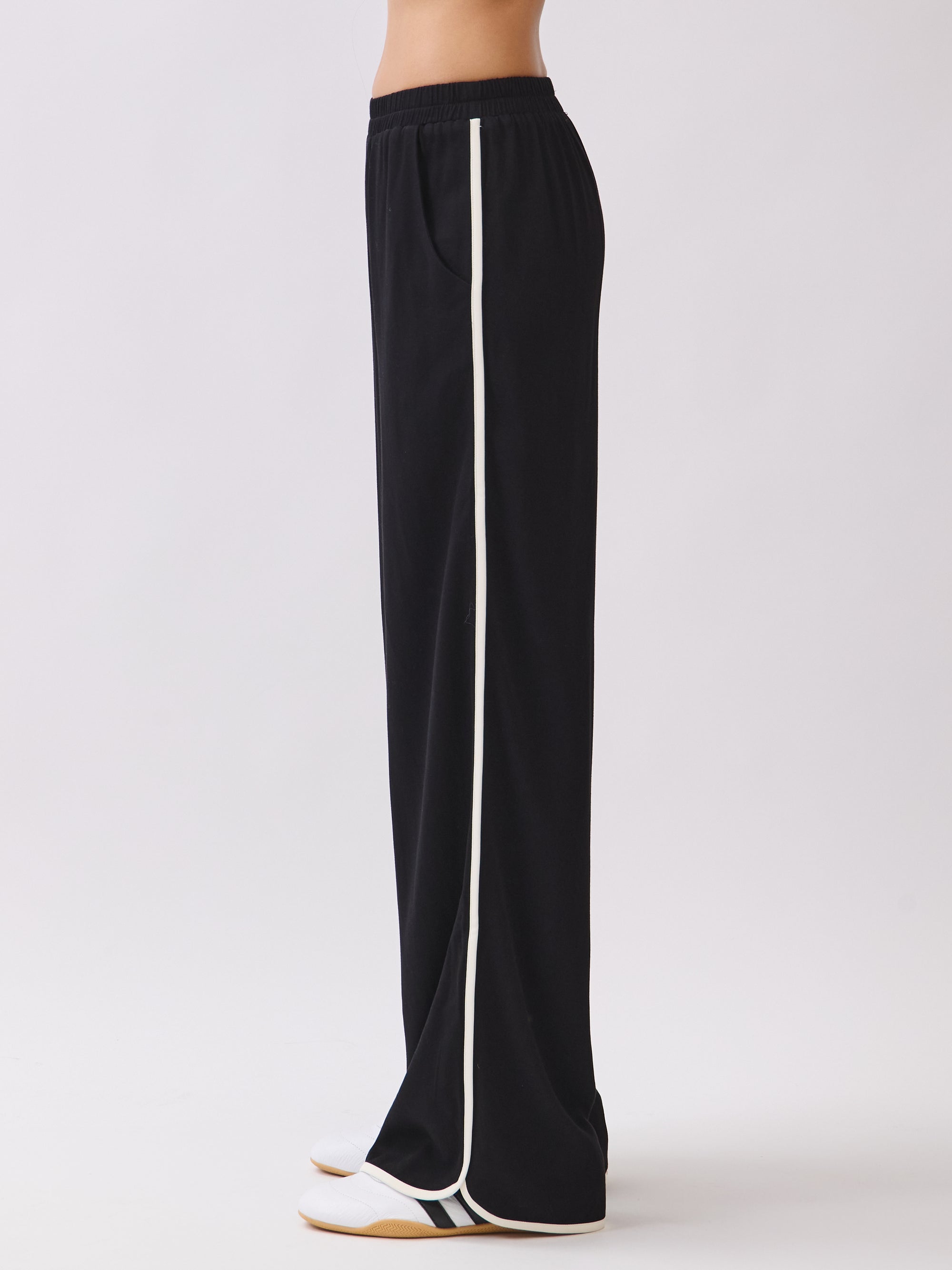 Side view of the Nova Contrast Trim Pants in black featuring white side piping and a relaxed straight-leg silhouette.