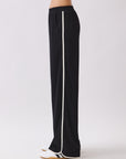 Side view of the Nova Contrast Trim Pants in black featuring white side piping and a relaxed straight-leg silhouette.