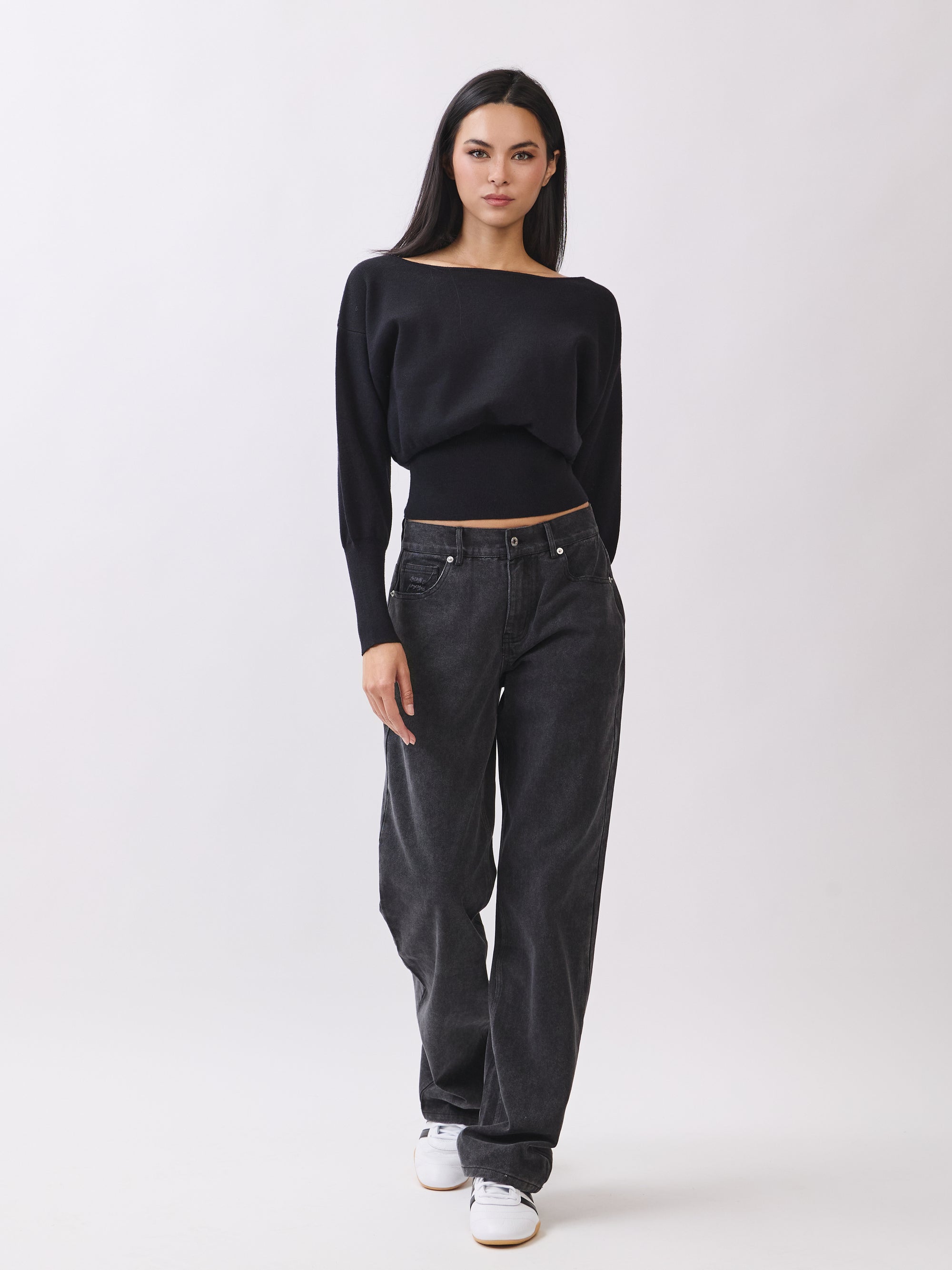 Model in BTTRMMT Black Tessa Boatneck Sweater with off-shoulder neckline and black jeans.