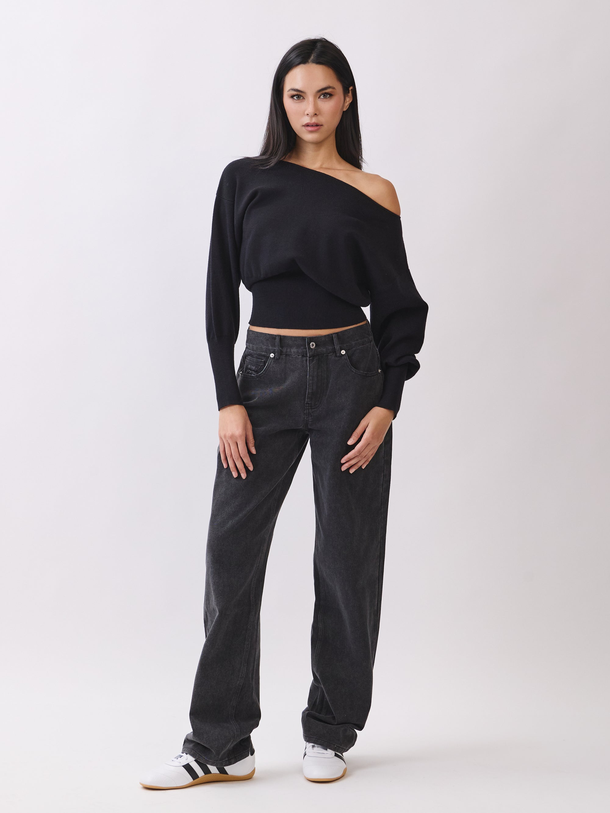 Model in BTTRMMT Black Tessa Boatneck Sweater with off-shoulder neckline and black jeans.