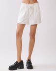 Model wearing BTTRMMT Cali Paperback Shorts in ivory with elastic paperbag waist, front pockets, and a drawstring tie.