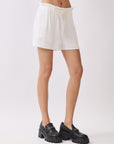 Side view of model wearing BTTRMMT Cali Paperback Shorts in ivory, featuring an elastic paperbag waist and relaxed fit.