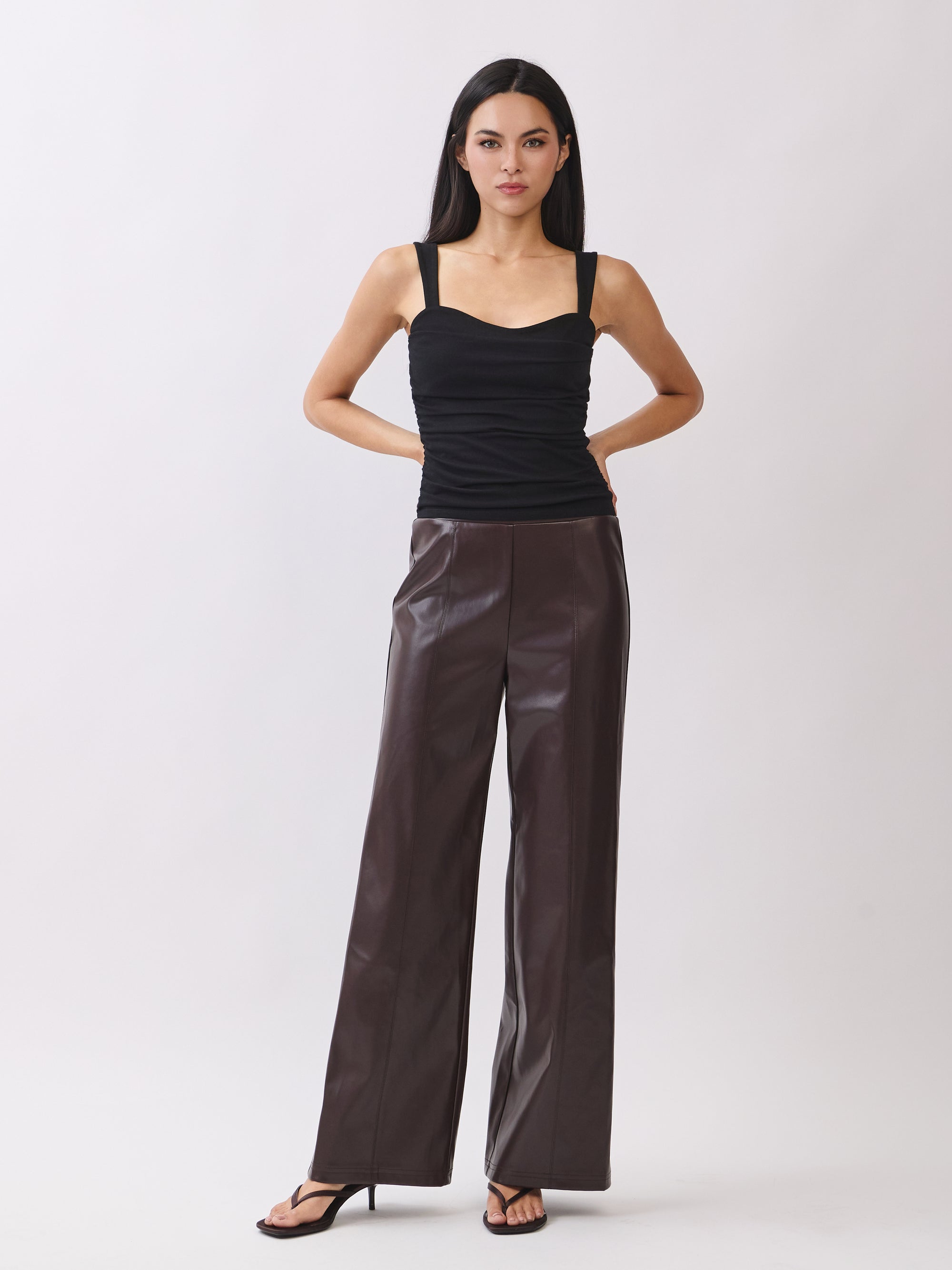 Model wearing BTTRMMT dark brown faux leather pants with straight-leg fit, paired with black ruched tank top.