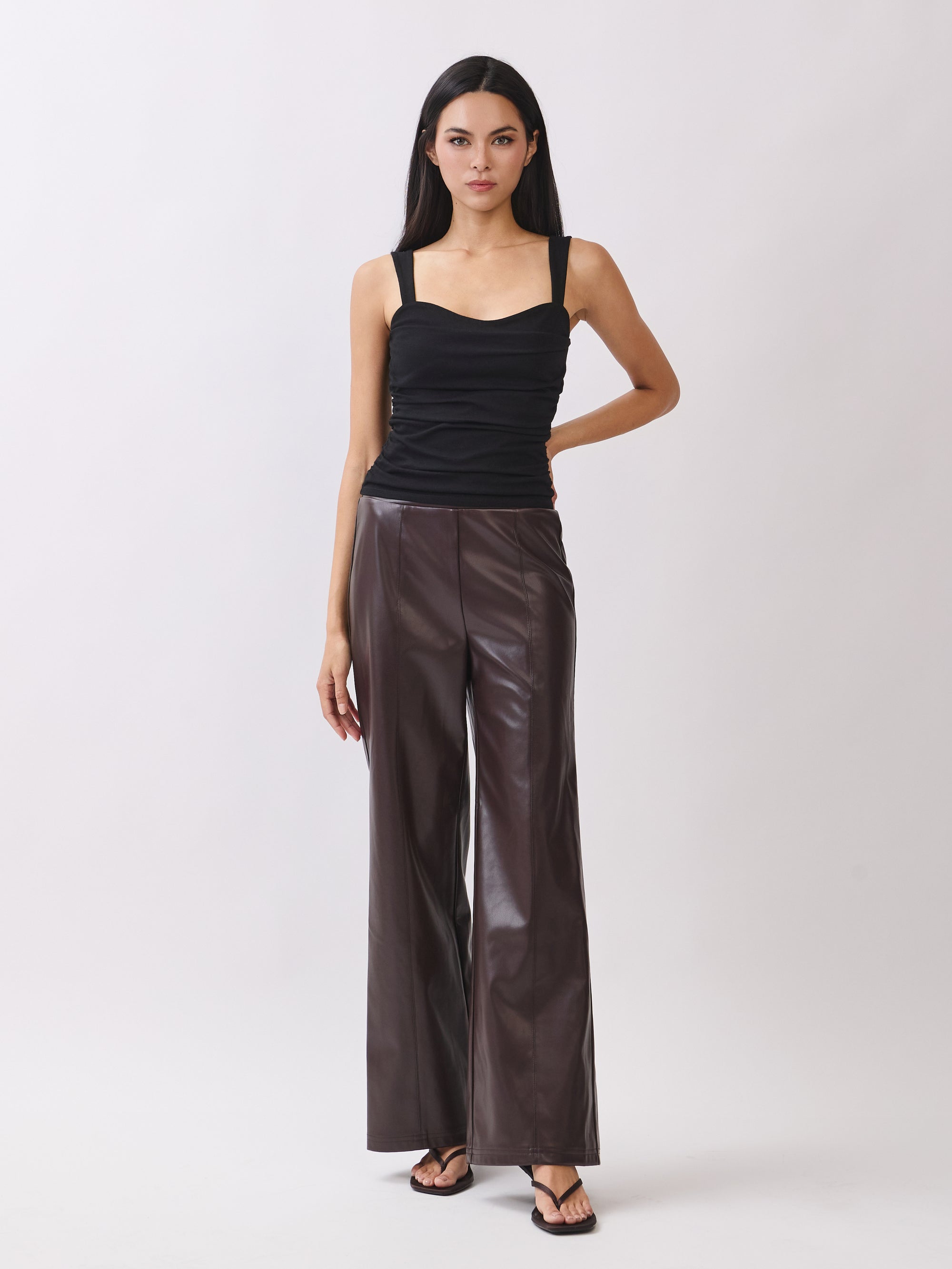 Model wearing BTTRMMT dark brown faux leather pants with straight-leg fit, paired with black ruched tank top.
