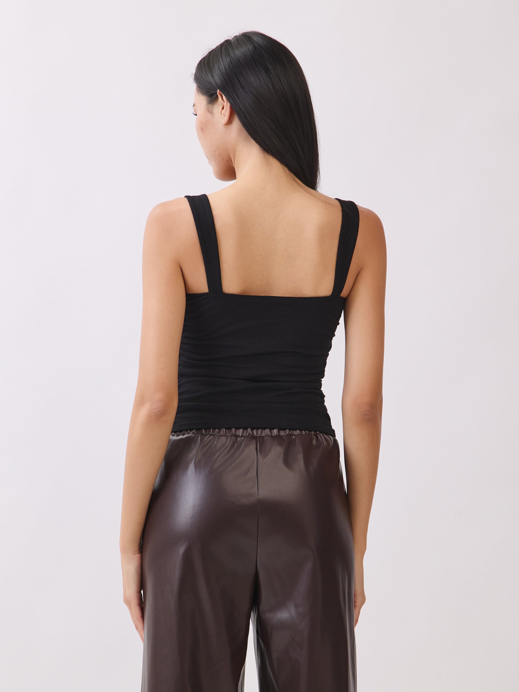 Back view of model wearing BTTRMMT The Brielle Top, a black ruched tank with wide straps, paired with brown faux leather pants.