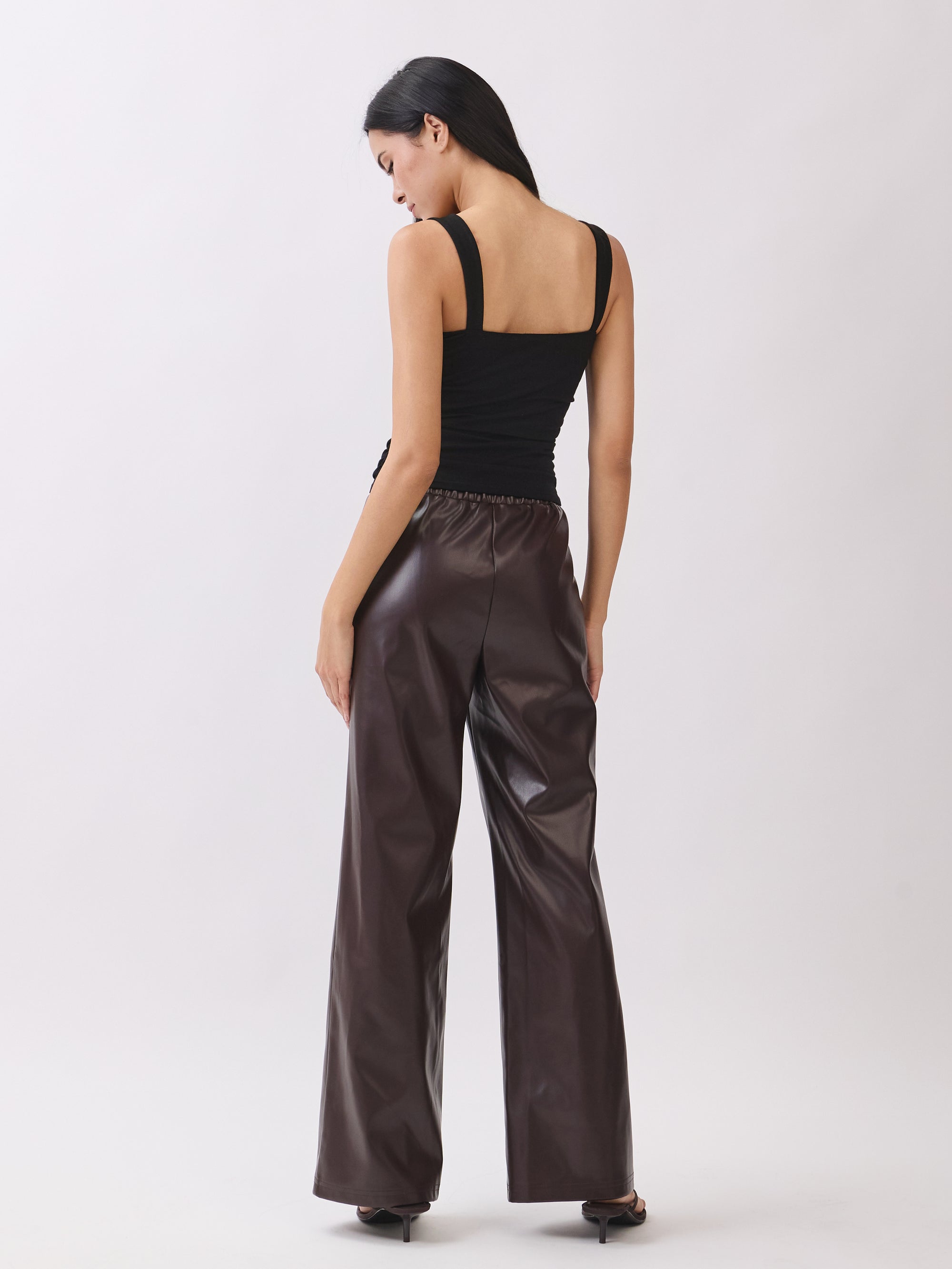 Back view of BTTRMMT dark brown faux leather pants with straight-leg fit and stitched seam detail.
