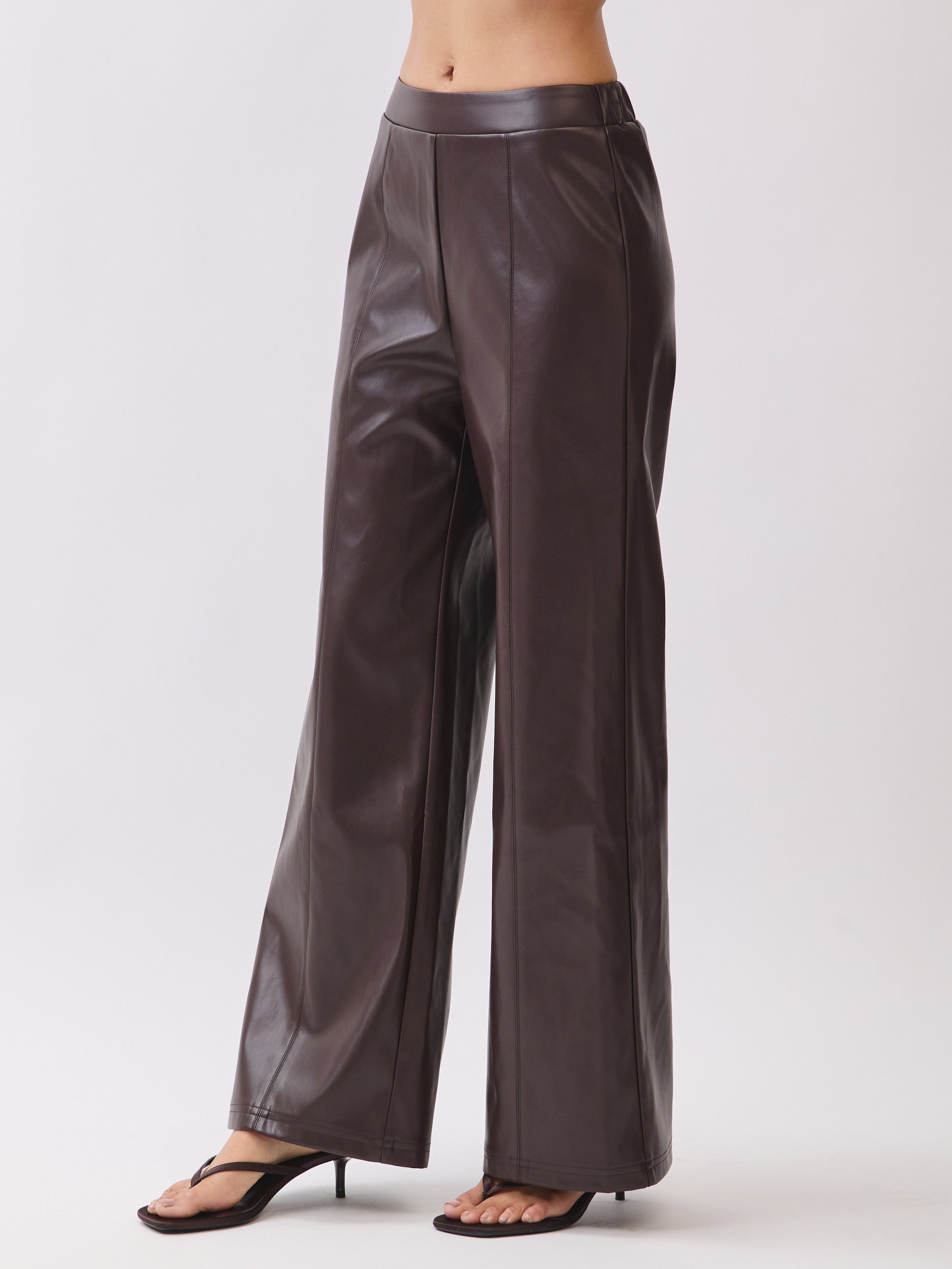 Side view of BTTRMMT dark brown faux leather pants with straight-leg fit and stitched seam detail.