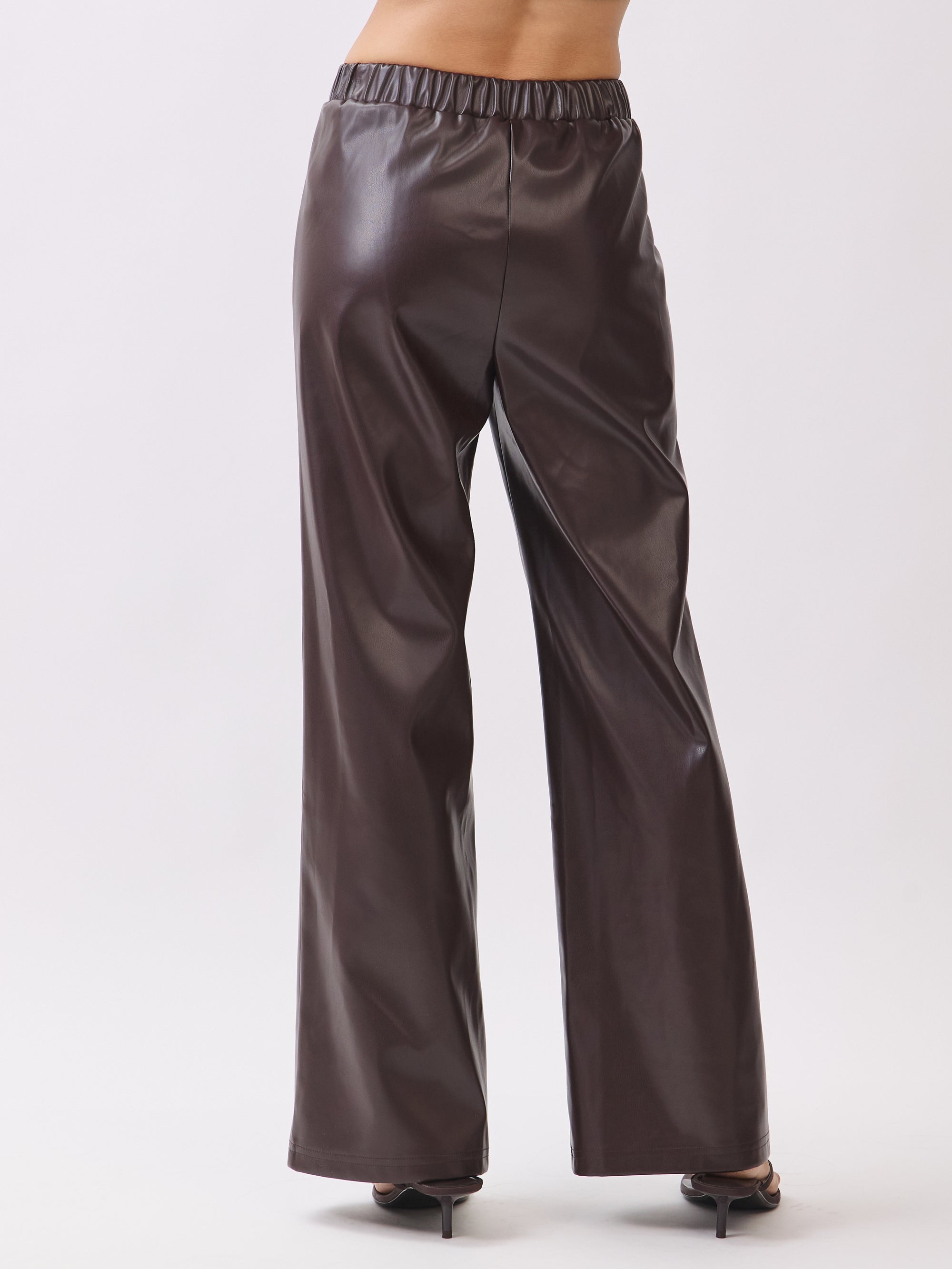 Back view of model wearing BTTRMMT dark brown faux leather pants with straight-leg fit and seam detail.