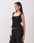 Side view of BTTRMMT black ruffle sleeveless top with tie detail, paired with black pants for a chic everyday look
