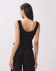Back view of BTTRMMT black ruffle sleeveless top showing gathered detail, styled with black pants for a clean minimal look