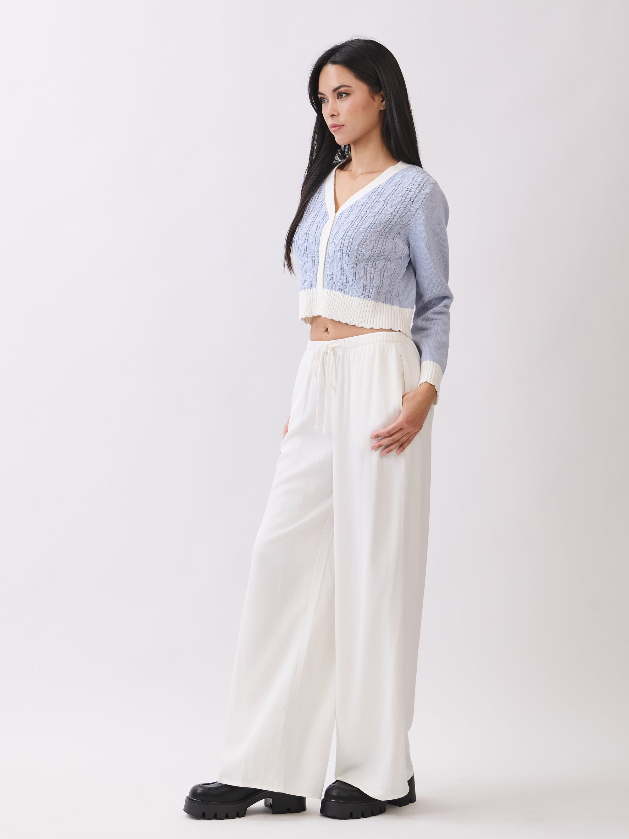 Side view of model wearing BTTRMMT Ivory Calia Pants with a relaxed wide-leg fit, paired with a cropped blue and white knit cardigan.