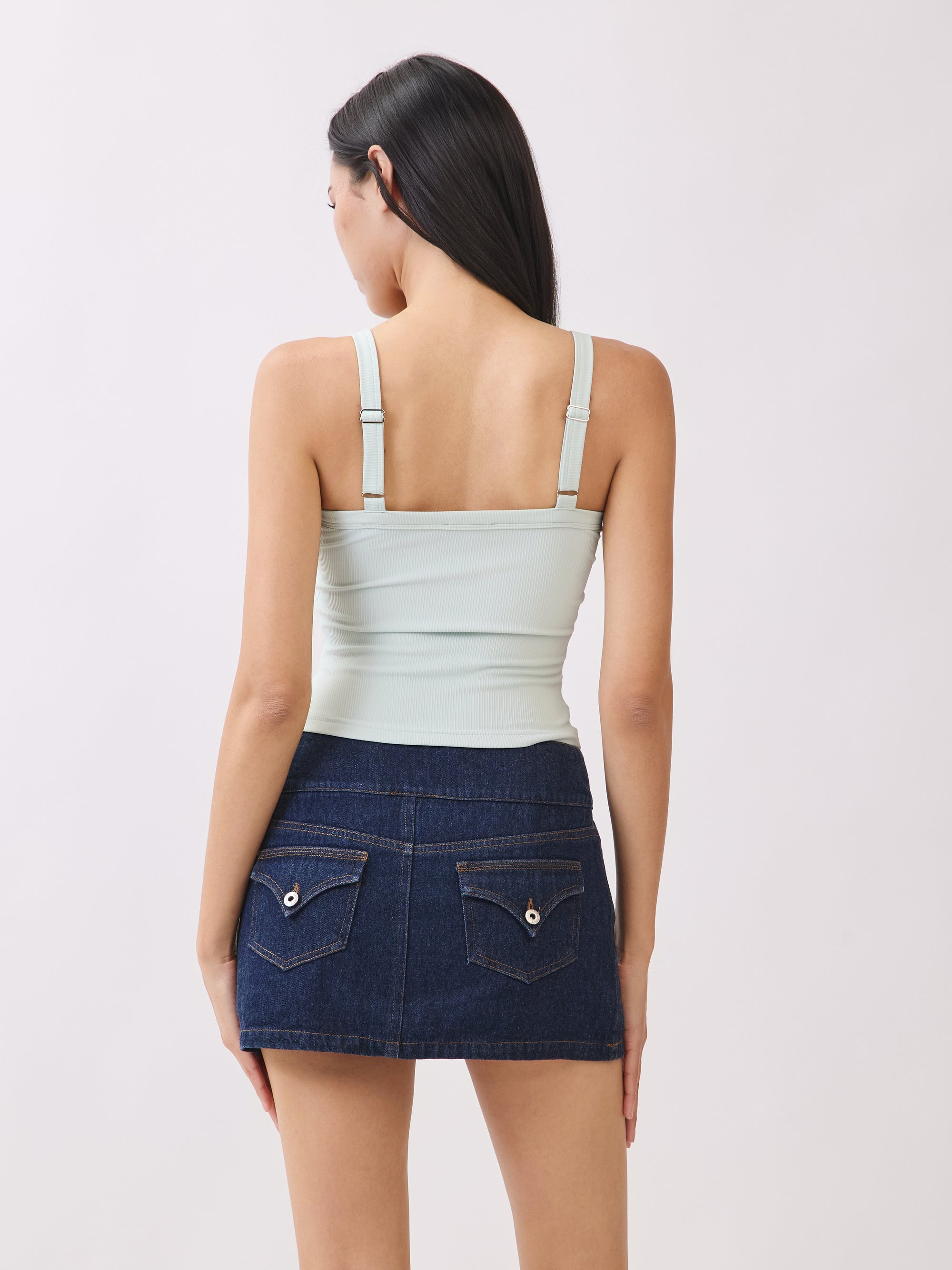 Back view of model wearing BTTRMMT mint cutout tank top with straps, paired with dark denim mini skirt.