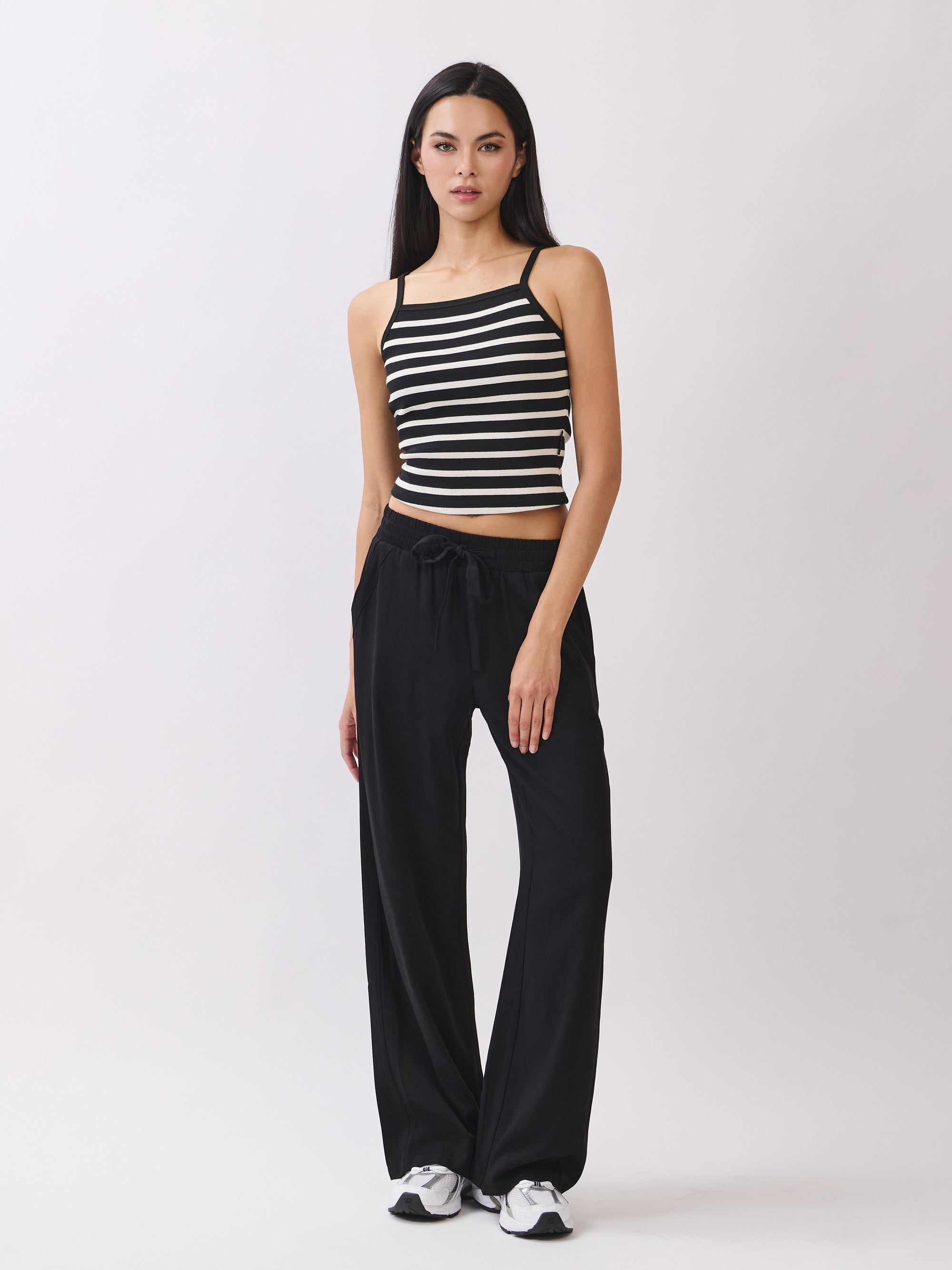 Model wearing BTTRMMT Black Yuna Soft Wide Leg Pants with drawstring waist and relaxed fit, paired with striped knit tank and sneakers.