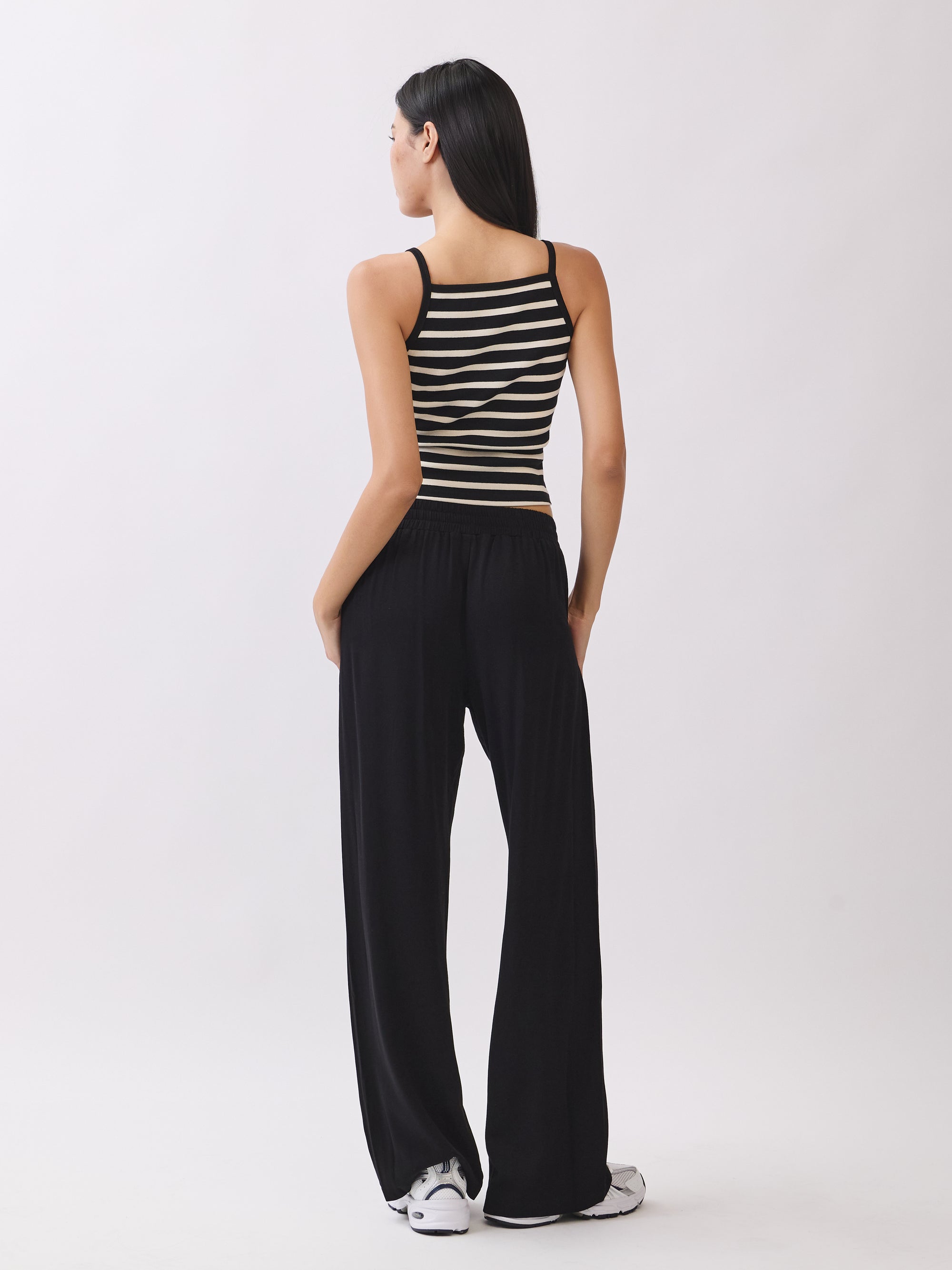 Back view of BTTRMMT Black Yuna Soft Wide Leg Pants with a drawstring waist and relaxed fit, styled with a striped knit tank and sneakers.
