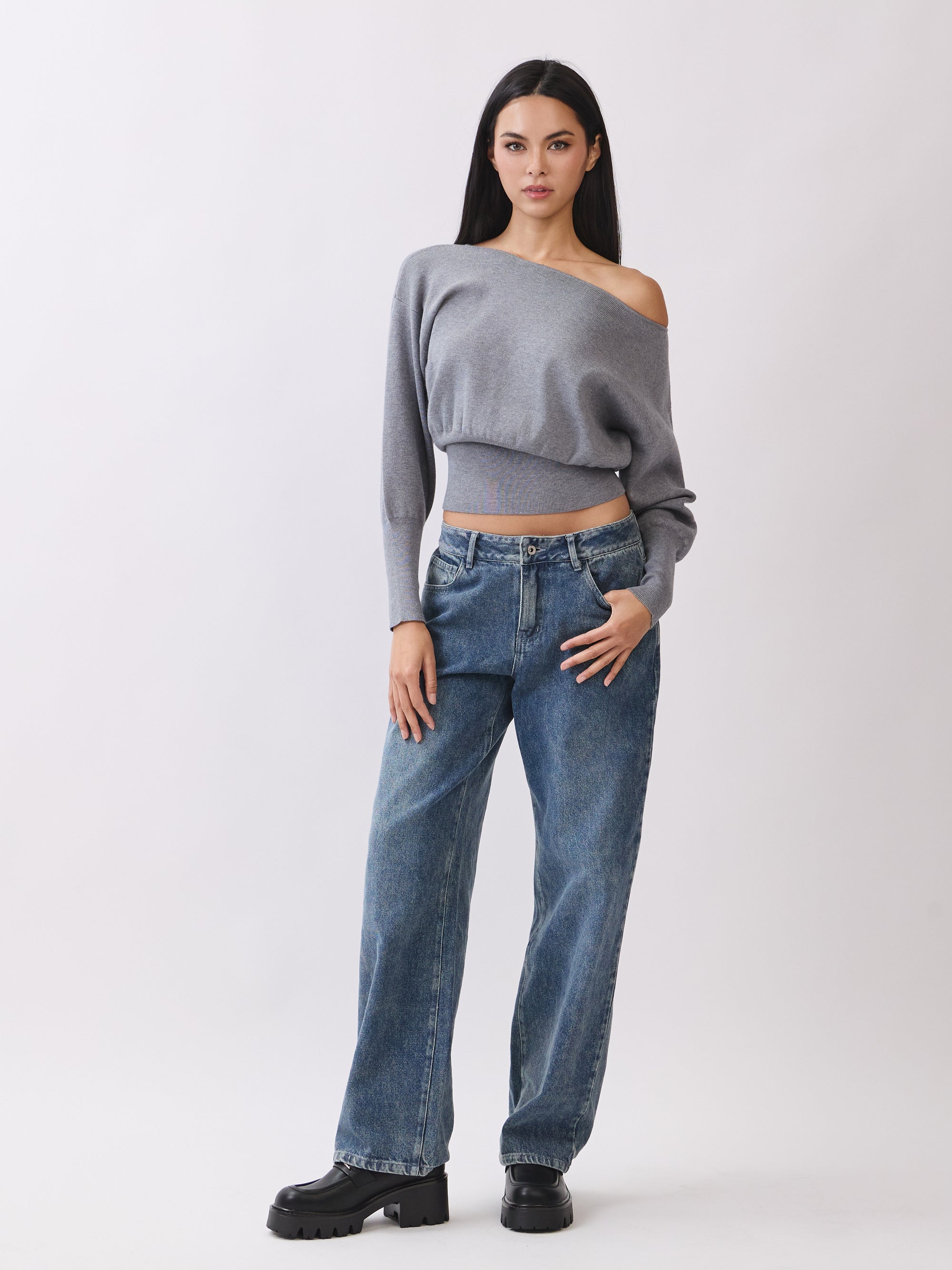 Model in BTTRMMT Gray Tessa Boatneck Sweater, off-shoulder knit with jeans and black boots.