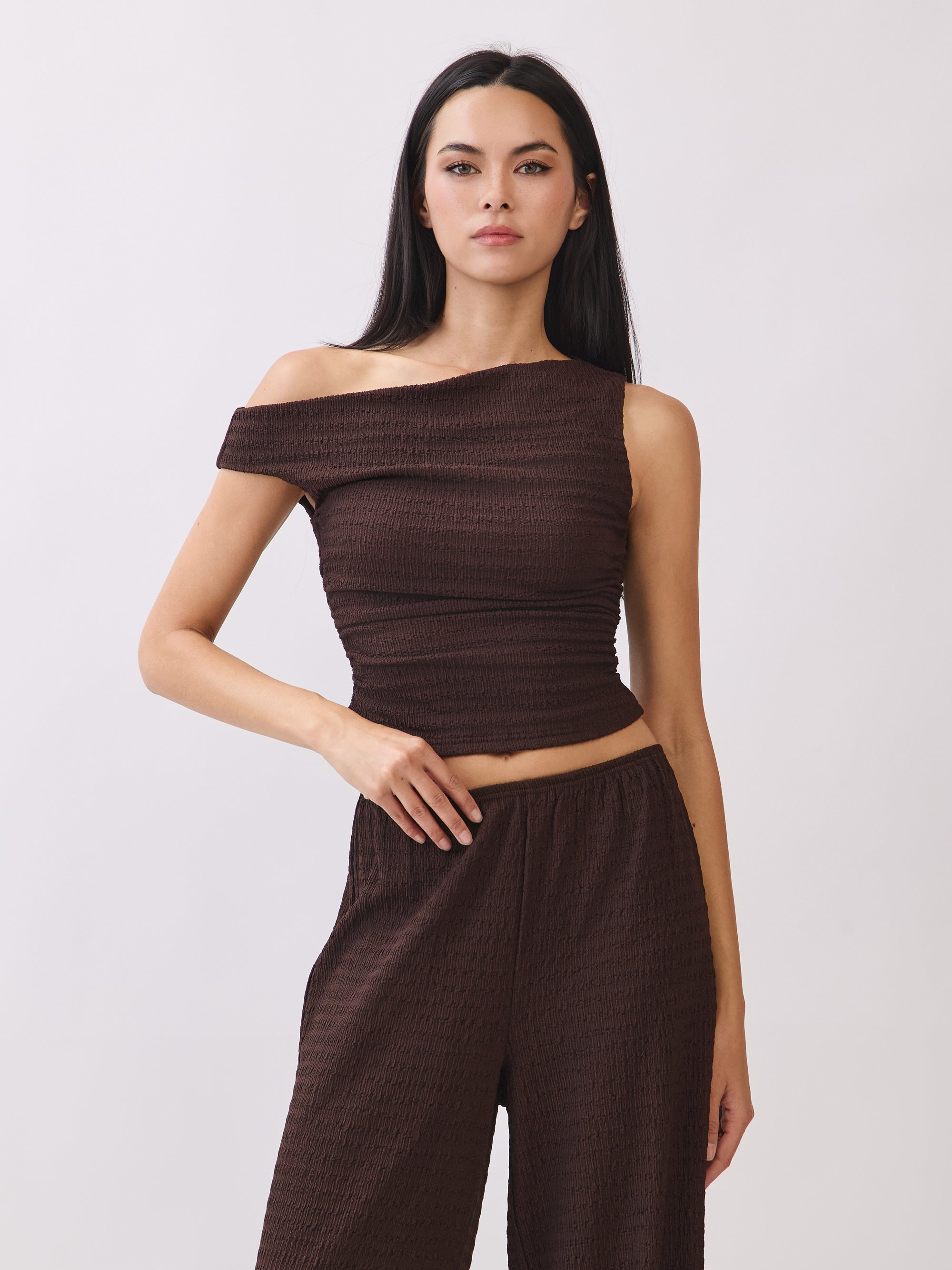 Model wearing the BTTRMMT Daniela Off-Duty Set in brown, featuring a one-shoulder ruched top and matching wide-leg pants for an elevated casual look.