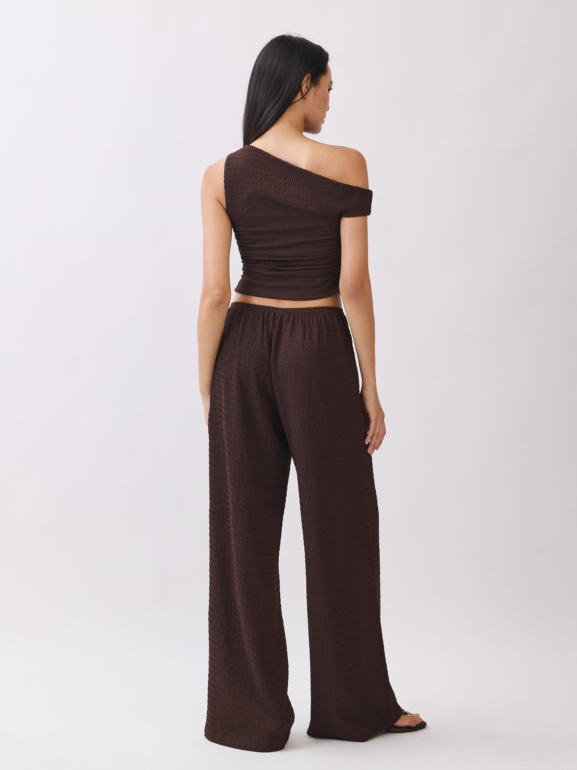 Back view of model wearing the BTTRMMT Daniela Off-Duty Set in brown featuring a fitted ruched back and matching wide-leg pants.