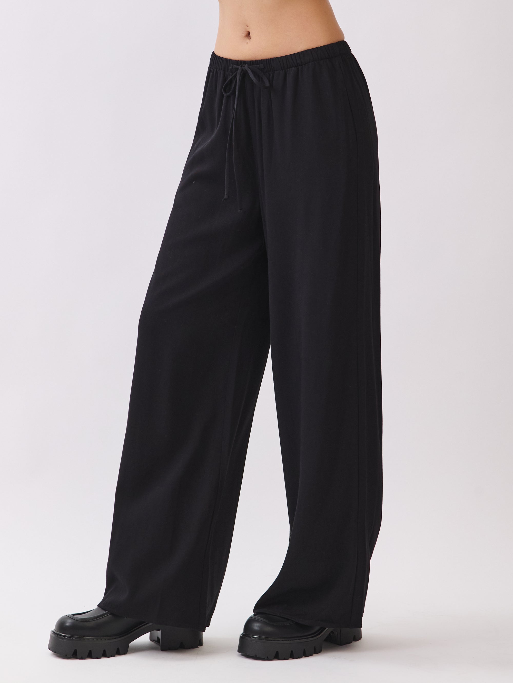 BTTRMMT black wide-leg drawstring pants shown from the side, featuring a relaxed drape and soft flowy fit for everyday comfort