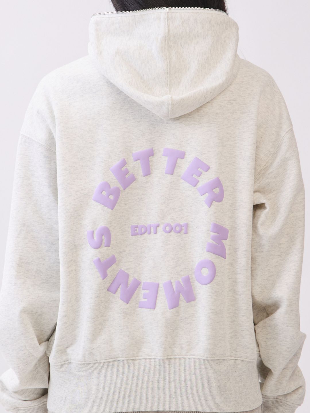 Model wearing BTTRMMT Chill Zip hoodie with lilac “Better Moments Edit 001” logo on the back, cozy minimal streetwear look.