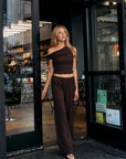 Model wearing the BTTRMMT Daniela Off-Duty Set in brown, in a one-shoulder ruched top and wide-leg pants.
