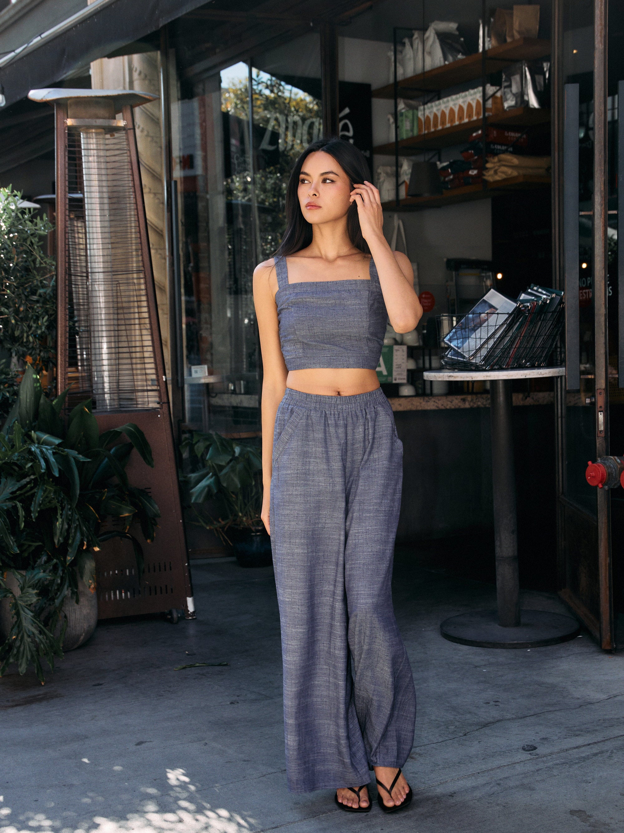 Model wearing BTTRMMT Denim Olivyn Set in blue, featuring cropped square-neck top and flowy wide-leg pants, standing outside a café.