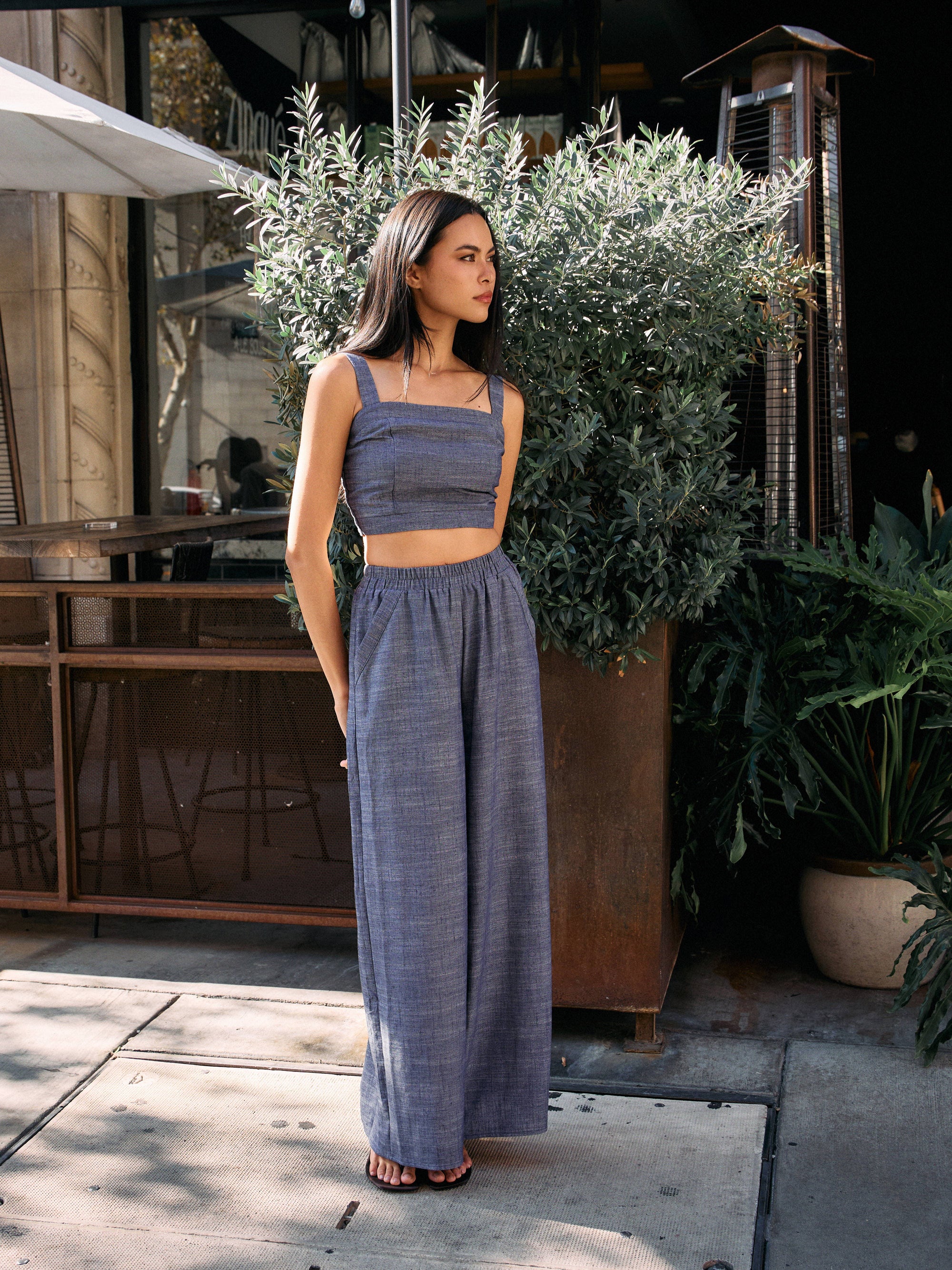 Model wearing BTTRMMT Denim Olivyn Set in blue with a cropped square-neck top and wide-leg pants while standing outside a café.