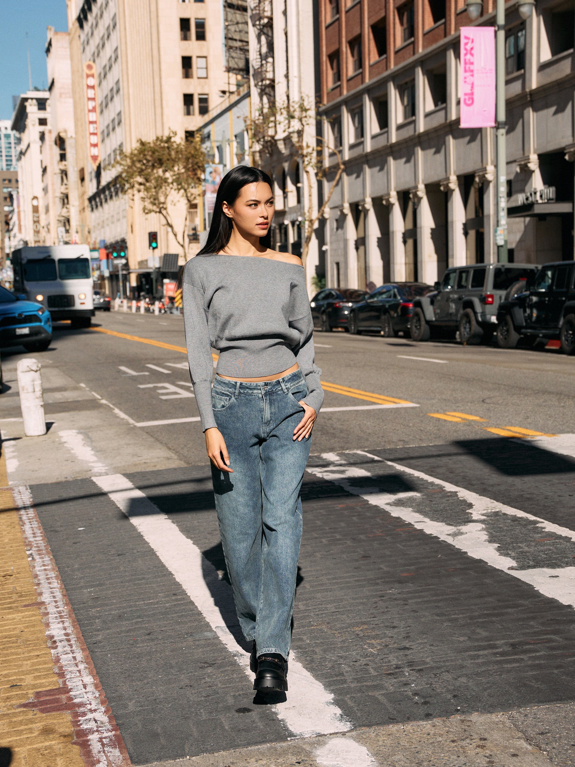 Model walking in BTTRMMT Gray Tessa Boatneck Sweater, off-shoulder knit with jeans and black loafer.