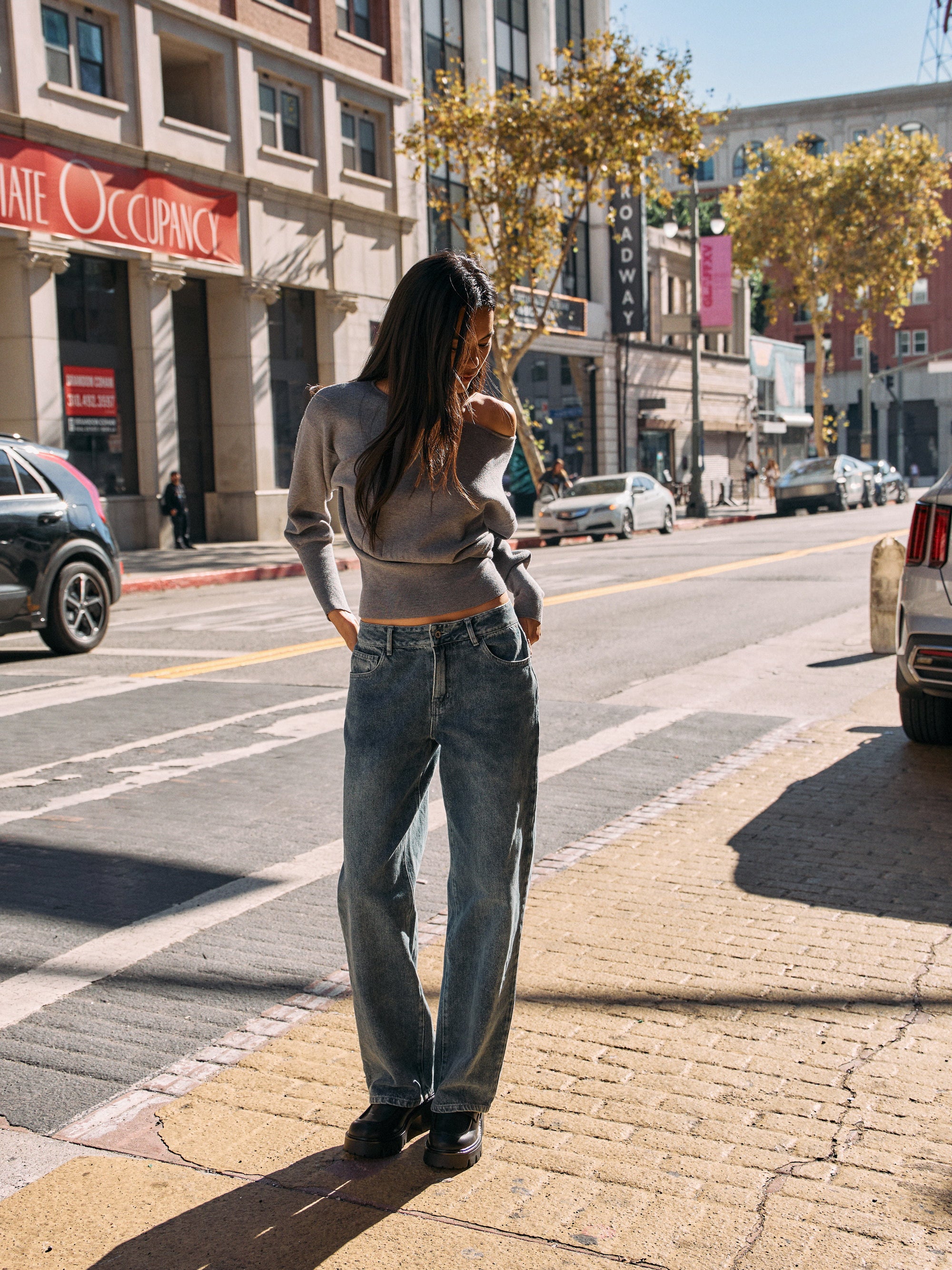 Model wearing BTTRMMT Drop Zone Low Rise Wide Leg Jeans in vintage blue, styled with a gray knit top while standing on a city street.