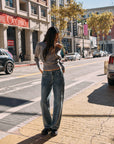 Model wearing BTTRMMT Drop Zone Low Rise Wide Leg Jeans in vintage blue, styled with a gray knit top while standing on a city street.