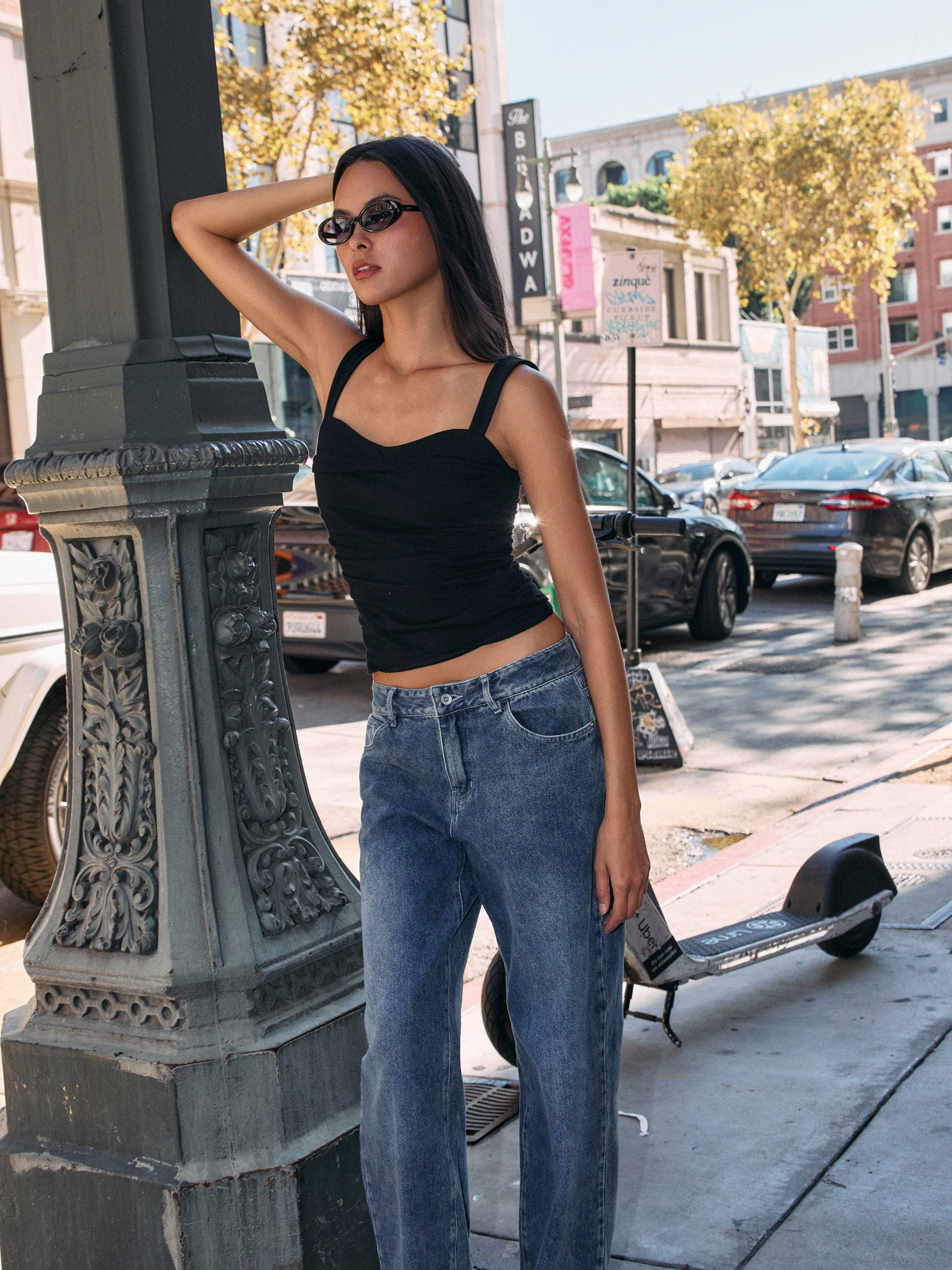 Model wearing BTTRMMT The Brielle Top, black ruched tank with wide straps and square neckline, styled with blue jeans outdoors.