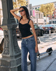 Model wearing BTTRMMT The Brielle Top, black ruched tank with wide straps and square neckline, styled with blue jeans outdoors.