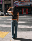 Model wearing BTTRMMT Drop Zone Low Rise Wide Leg Jeans in vintage blue, styled with a gray knit top while standing on a city street.