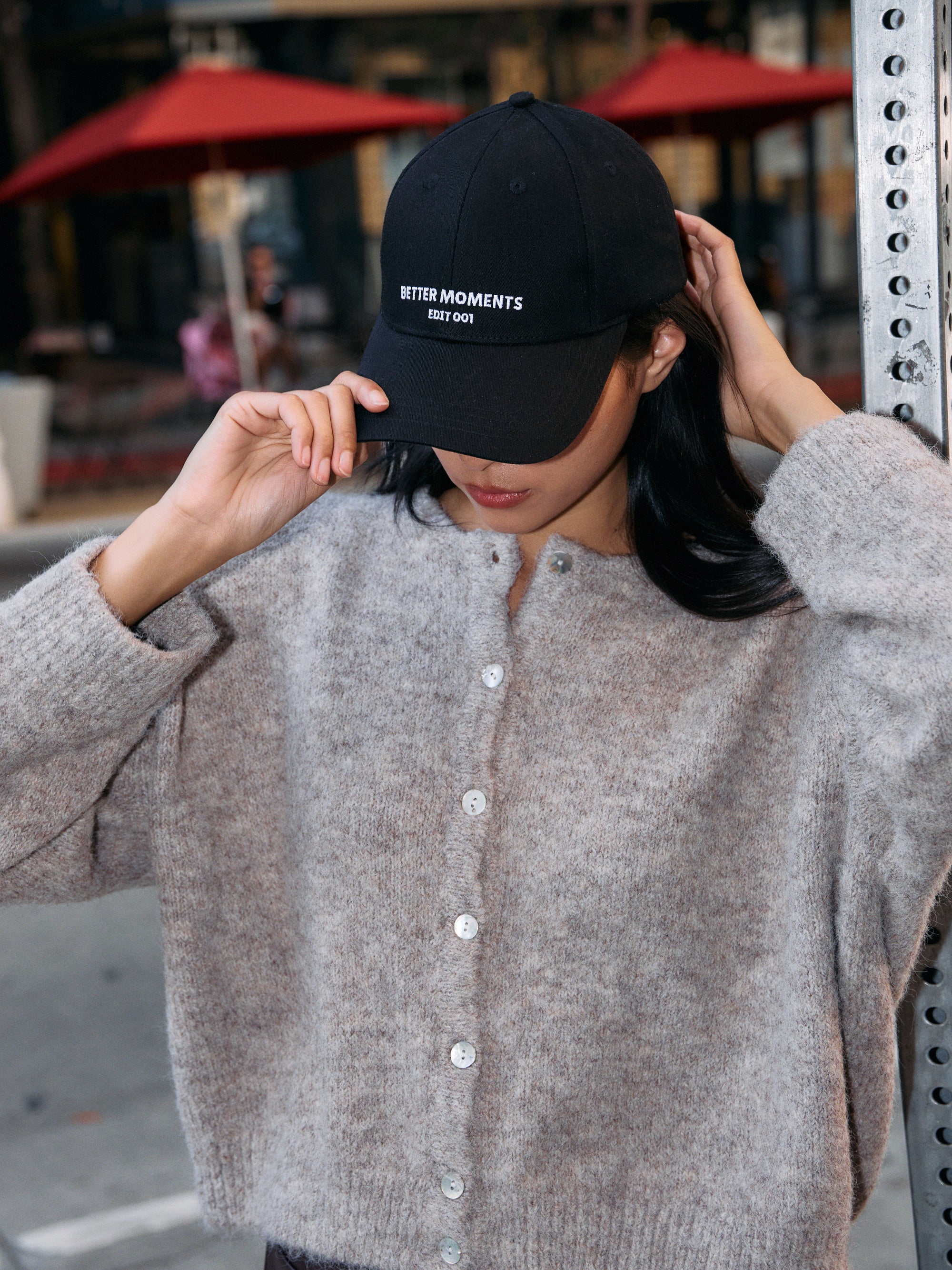 BTTRMMT black Better Moments cap styled with a soft taupe button-up cardigan during a casual city moment."