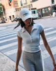 BTTRMMT white crop polo top and gray ribbed pants styled with the BTTRMMT Better Moments cap while walking in the city.