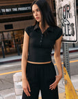 BTTRMMT Black Eliza Fitted Polo Top styled outdoors, showing its sleek stretch fit, cap sleeves, and flattering cropped silhouette.