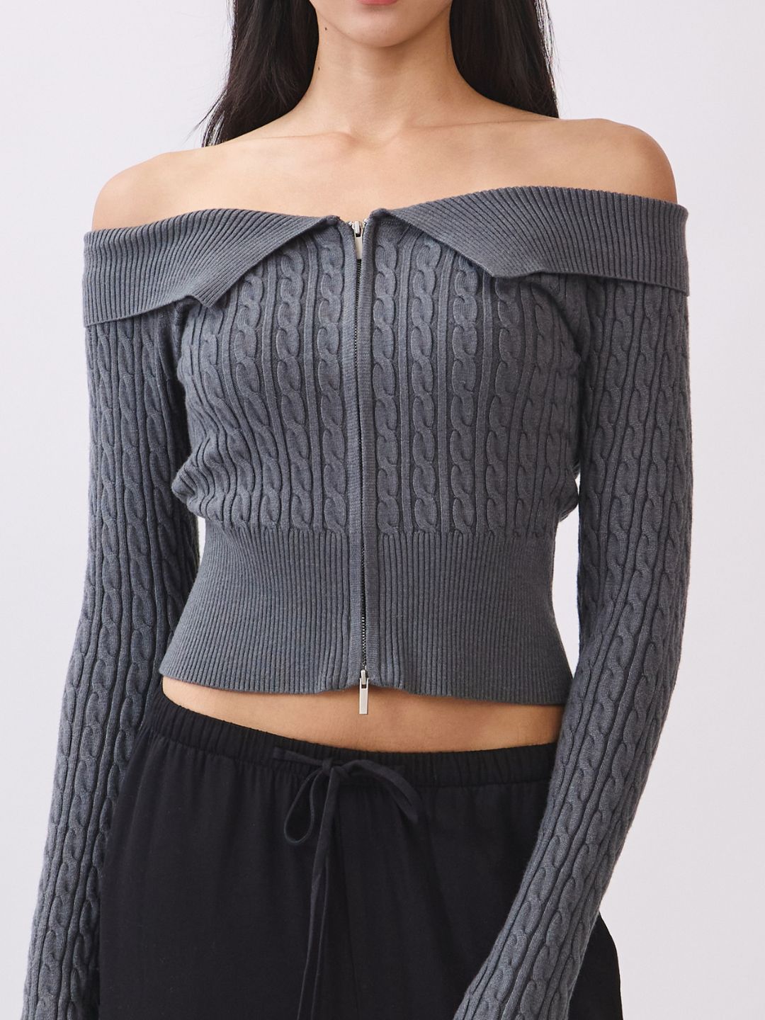Model wearing the BTTRMMT Camille Zip Knit in charcoal gray, an off-shoulder ribbed zip-up sweater with a fitted cropped silhouette.