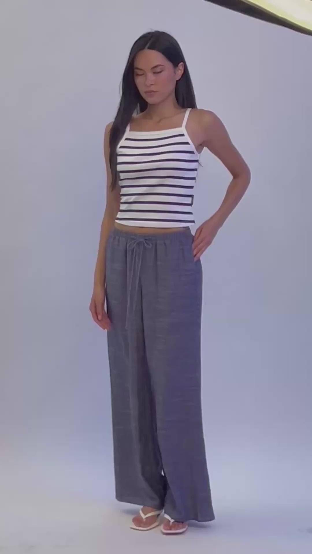 Model in studio wearing BTTRMMT Denim Calia Pants with drawstring waist and wide-leg fit, paired with a striped knit tank.